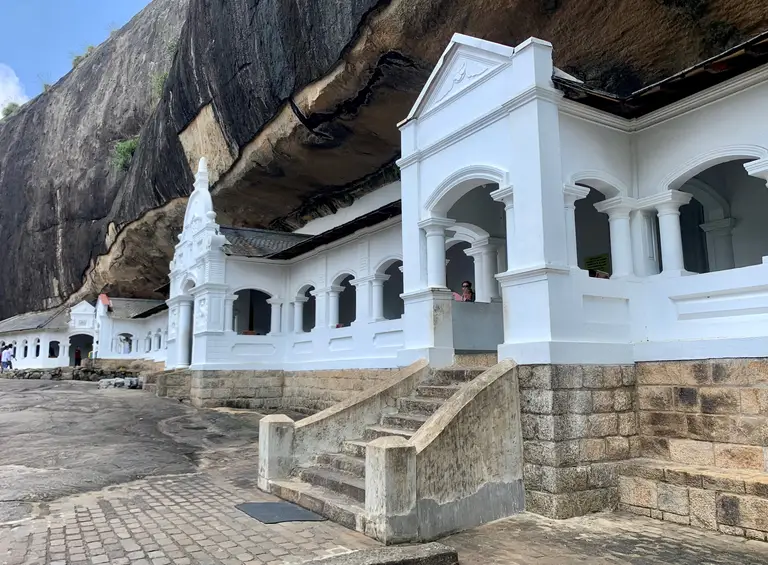 The white exterior of Dambulla Cave Temple beneath the rock overhang